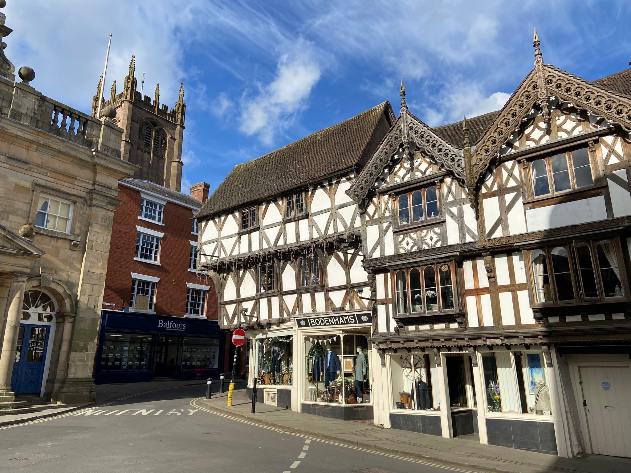 The Bodenhams of Ludlow shopfront on Broad Street, a timber-framed Tudor building with the BODENHAMS signage panel above the bay windows, with the tower of St Laurence's church and the Buttercross of Ludlow behind